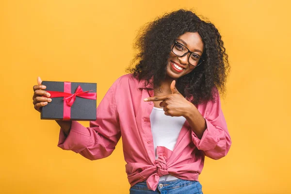 Happy african american lady in casual looking aside and laughing while holding present isolated over yellow background.
