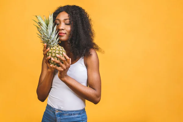 Pineapple exotic midfielder in a diet. The african american black dark-skinned cheerful girl holds in her hands the pineapple isolated over yellow background.