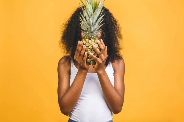 Pineapple exotic midfielder in a diet. The african american black dark-skinned cheerful girl holds in her hands the pineapple isolated over yellow background.