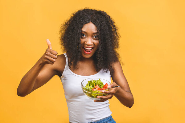 Healthy food concept. Close-up Of Beautiful African American black Woman Eating Salad isolated over yellow background. Thumbs up.