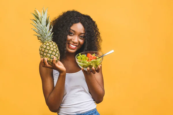 Healthy food concept. Close-up Of Beautiful African American black Woman Eating Salad and pineapple  isolated over yellow background.