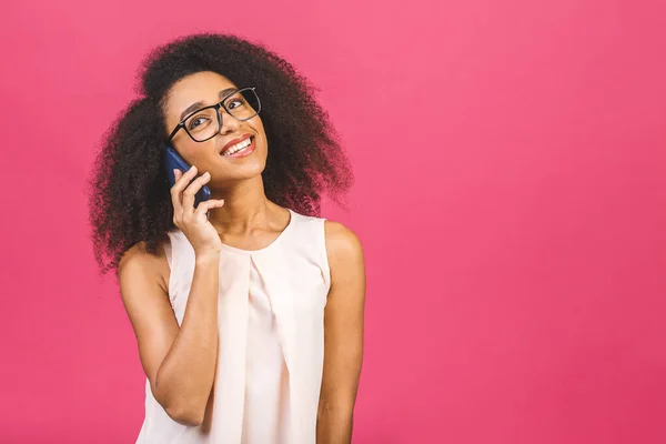 Portrait of a cute happy afro american black girl in casual talking on mobile phone and laughing isolated over pink background.