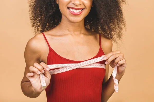 Dieting concept. Slim shocked amazed african american woman shows centimeter isolated over beige background.