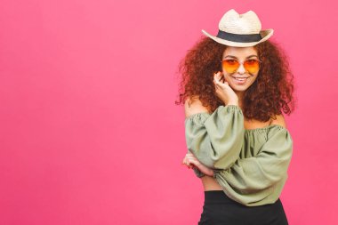 Seyahat yaz konsepti. Hasır şapkalı şık kıvırcık kız ya da kadın. Pembe arka planda izole edilmiş güneş gözlüğü ve fotokopi alanı var.. 