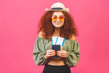 Seyahat yaz konsepti. Hasır şapkalı şık kıvırcık kız ya da kadın. Pembe arka planda izole edilmiş güneş gözlüğü ve fotokopi alanı var. Uçak bileti tutuluyor..