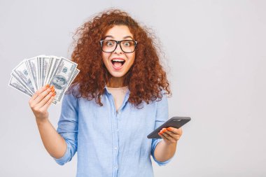 Beyaz arka planda izole bir şekilde duran, elinde para banknotları tutan, cep telefonu kullanan kıvırcık, güzel bir kızın portresi..