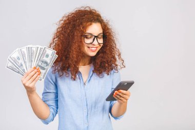 Beyaz arka planda izole bir şekilde duran, elinde para banknotları tutan, cep telefonu kullanan kıvırcık, güzel bir kızın portresi..