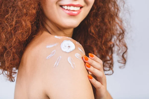 Young beautiful woman with sun-shaped sun cream. Pretty woman ready for suntan treatment. Sunscreen lotion sun drawing on woman shoulder. Isolated on white background.