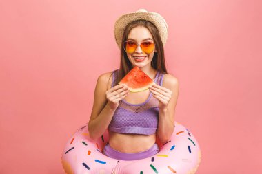 Mayo giymiş, atlayan ve pembe arka planda izole bir şekilde yüzen genç bir kadının portresi. Karpuz tutarken.