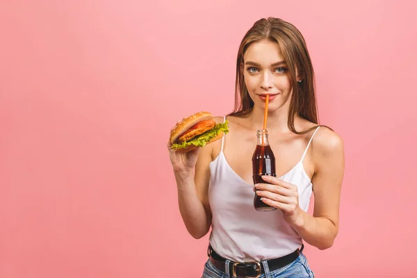 若い美しい空腹の女性の肖像バーガーを食べている ピンクを背景にファーストフードを持つ学生の孤立した肖像画 国会の概念 — ストック写真