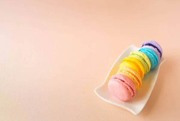 Resmin sağ tarafındaki beyaz dikdörtgen tabakta duran altı farklı renkte el yapımı badem kurabiyesi içeren minimalist kompozisyon. Pembe, mavi, açık yeşil, sarı, mor ve turuncu kurabiyeler.