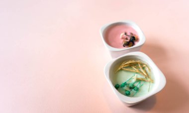 Mavi kağıt bir karenin üzerinde iki el yapımı, mavi ve pembe mum bulunan minimalist kompozisyon. Açık pembe arkaplanda kağıt desenli nesneler. El yapımı mumlar doğal yollardan yapılır.