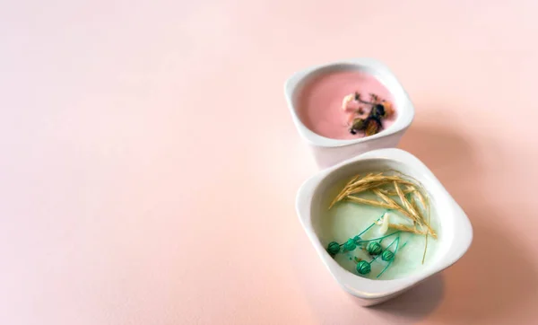 Mavi kağıt bir karenin üzerinde iki el yapımı, mavi ve pembe mum bulunan minimalist kompozisyon. Açık pembe arkaplanda kağıt desenli nesneler. El yapımı mumlar doğal yollardan yapılır.