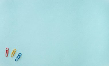 Açık mavi arkaplanda mavi, sarı ve kırmızı ataçların yatay minimalistik düz bileşimi. Eşyalar sol alt köşede. Ofis malzemeleri konsepti. Kırtasiye malzemeleri. Yatay