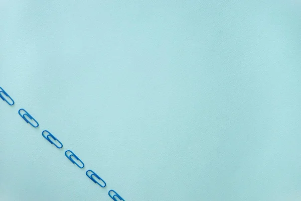 Açık mavi bir arkaplanda mavi ataçların yatay minimalistik düz kompozisyonu. Eşyalar sol alt köşede. Nesneler çapraz konumda. Ofis malzemeleri konsepti