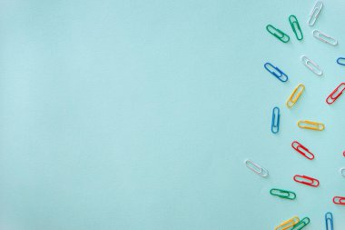 Açık mavi arkaplanda çok renkli ataçların yatay minimalistik düz kompozisyonu. Fotoğrafın sağ tarafında yeşil, kırmızı, sarı, beyaz ve mavi nesneler var.