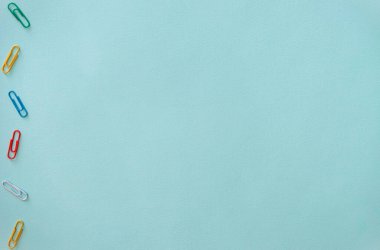 Açık mavi arkaplanda çok renkli ataçların yatay minimalistik düz kompozisyonu. Fotoğrafın sol tarafında yeşil, kırmızı, sarı, beyaz ve mavi nesneler var.