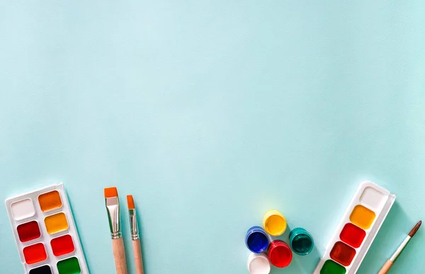 Yatay yakın çekim düz kompozisyonu, turuncu ve ahşap desenli iki açık bej fırça, beyaz kazıklı bir fırça, iki set suluboya boya ve beş gouache boya.