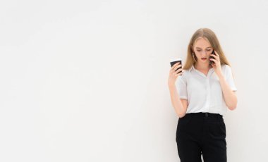 Beyaz bir duvarın önünde duran beyaz saçlı genç bir iş kadınının portresi telefonla konuşuyor, aşağı bakıyor, düşünüyor ve elinde kahve tutuyor. O, siyah pantolon ve kısa kollu beyaz bir gömlek giydi. Başarılı olma kavramı