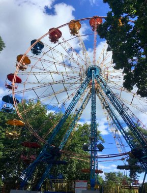 Bir yaz parkında ağaçların arasında gökyüzüne karşı dönen dönme dolaba sahip şehir manzarası
