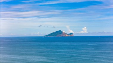 Işıl ışıl bir yaz gökyüzünün altında derin mavi denizden yükselen yalnız bir ada.