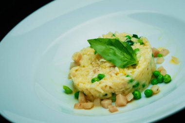 Beyaz tabakta kelebek, ıspanak ve yeşil bezelye ile risotto.