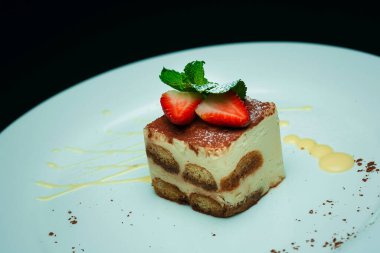 Beyaz tabakta tiramisu keki, nane yaprağı ve çilek.