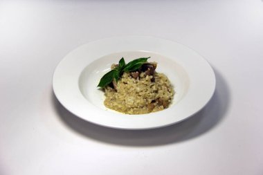 Beyaz tabakta mantarlı pilav ve fesleğen yaprağı.