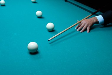 Bilardo oyunu elinde bilardo ıstakası olan bir adamın eli bilardo topunu hedef alır.