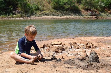 Yoğun bakışlı bir çocuk nehir kıyısında kale inşa eder..