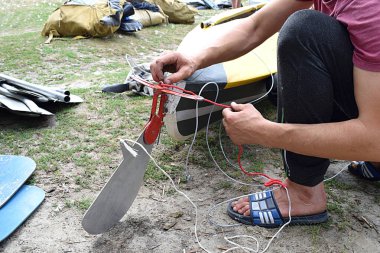 a man mounts a steering wheel on a kayak on the river bank before launching clipart