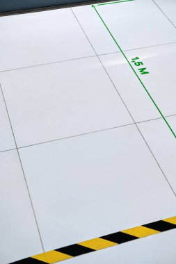 Yerdeki siyah ve sarı şeritli bant mesafeyi koruman gerektiğini gösteriyor. Yeşil çizgi işareti 1,5 metre, enfeksiyon kapmamak için Covid-19. 