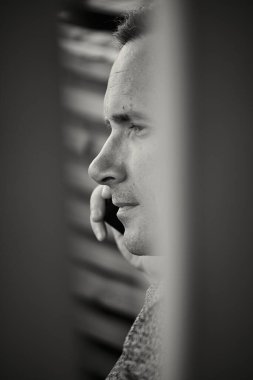Kafkasyalı beyaz sakin bir adamın tek renkli görüntüsü. Sevdiği biriyle cep telefonuyla konuşuyor. Tahtaların arasındaki boşluktan hayal et. Siyah beyaz fotoğraf..