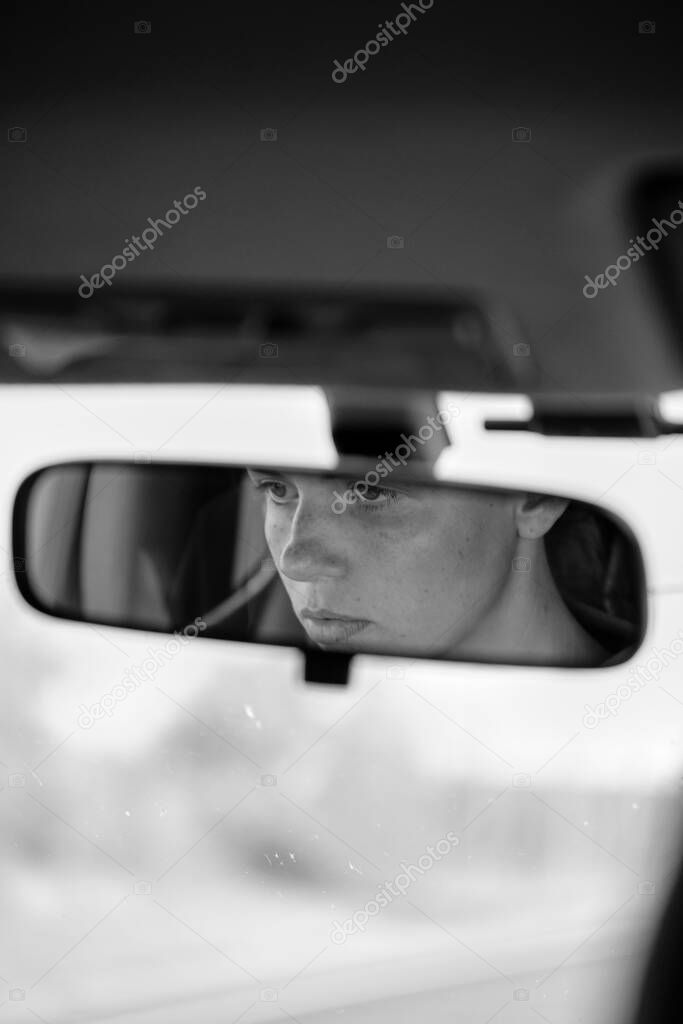Reflection of young female face and eyes in rearview mirror of a car. Woman driver.