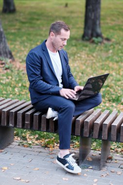 İşadamı mavi giyinmiş sıradan bir süit dizüstü bilgisayarla çalışıyor. Emlakçı parktaki ahşap bankta oturuyor ve işini yapıyor. Serbest meslek sahibi ve serbest meslek sahibi insanlar kavramı.