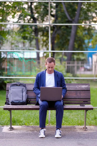 İşadamı mavi giyinmiş sıradan bir süit dizüstü bilgisayarla çalışıyor. Broker parktaki ahşap bankta oturuyor ve işini yapıyor. Aklında borsa çizelgeleri var. Serbest çalışma ve serbest çalışma kavramı.