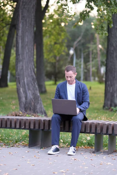 İşadamı mavi giyinmiş sıradan bir süit dizüstü bilgisayarla çalışıyor. Emlakçı parktaki ahşap bankta oturuyor ve işini yapıyor. Serbest meslek sahibi ve serbest meslek sahibi insanlar kavramı.