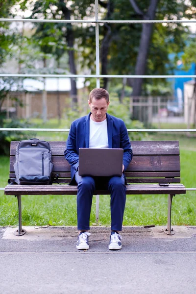 İşadamı mavi giyinmiş sıradan bir süit dizüstü bilgisayarla çalışıyor. Emlakçı parktaki ahşap bankta oturuyor ve işini yapıyor. Serbest meslek sahibi ve serbest meslek sahibi insanlar kavramı.