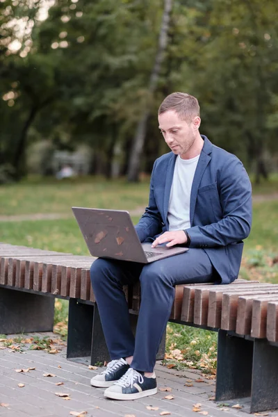 İşadamı mavi giyinmiş sıradan bir süit dizüstü bilgisayarla çalışıyor. Emlakçı parktaki ahşap bankta oturuyor ve işini yapıyor. Serbest meslek sahibi ve serbest meslek sahibi insanlar kavramı.