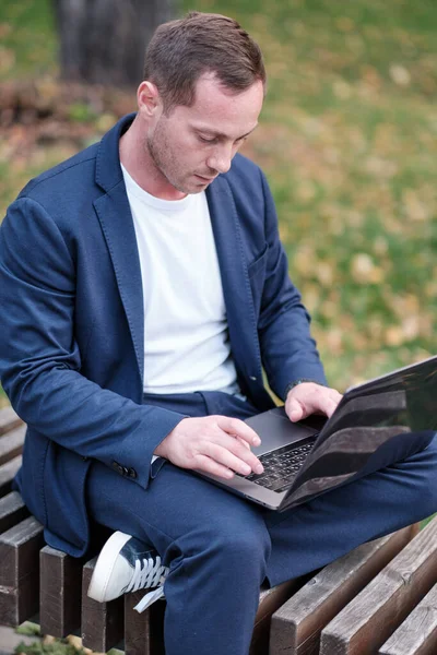 İşadamı mavi giyinmiş sıradan bir süit dizüstü bilgisayarla çalışıyor. Emlakçı parktaki ahşap bankta oturuyor ve işini yapıyor. Serbest meslek sahibi ve serbest meslek sahibi insanlar kavramı.