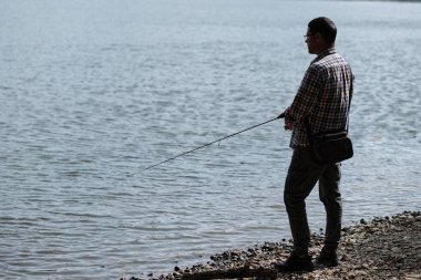 Balıkçı elinde olta tutarak balık yakalar. Şehirde spor, hobi ve boş zaman kavramı.