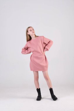 Stüdyo siklonamasında poz veren pembe büyük beden elbiseler ve siyah botlar giyen genç bir manken. Kıyafet reklamı kavramı.