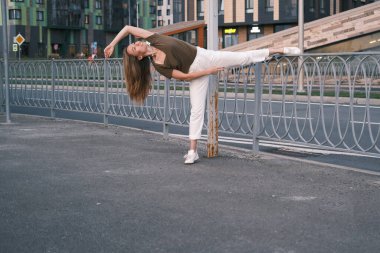 Beyaz pantolon ve zeytin tişörtü giymiş güzel Asyalı kadın dans ediyor ve sokakta esniyor. Boşluğu kopyala.