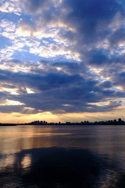 Arka plan olarak dramatik akşam gökyüzü üzerinde nehir manzarası. Sudaki bulutların yansıması..