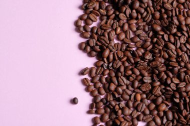 Arka plan olarak pembe renkli yüzeyde kavrulmuş ve aromatik kahve çekirdekleri. Üst görünüm ve metin için boşluk kopyala. Taze Arabika kahvesinin makro fotoğrafı....