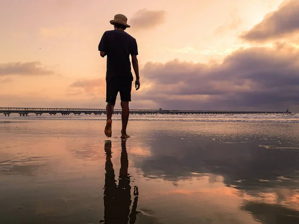 桟橋の前の夕日のビーチを歩く男のシルエット — ストック写真