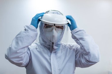 Beyaz biyo-koruma kıyafeti, yüz kalkanı, maske ve eldiven giyen bir doktor.