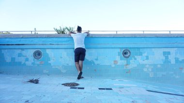 Sırtı mavi arka plana bakan bir adam boş bir havuzun içinde.