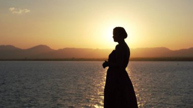 Genç bir kadının gölgesi denizin üzerinde gün batımına karşı.