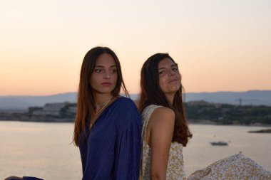 Gün batımında sırtı denize dönük iki arkadaş.